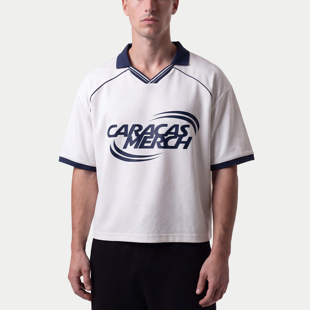 Hombre llevando la camiseta de fútbol boxy blanca de Caracas Merch con cuello azul marino